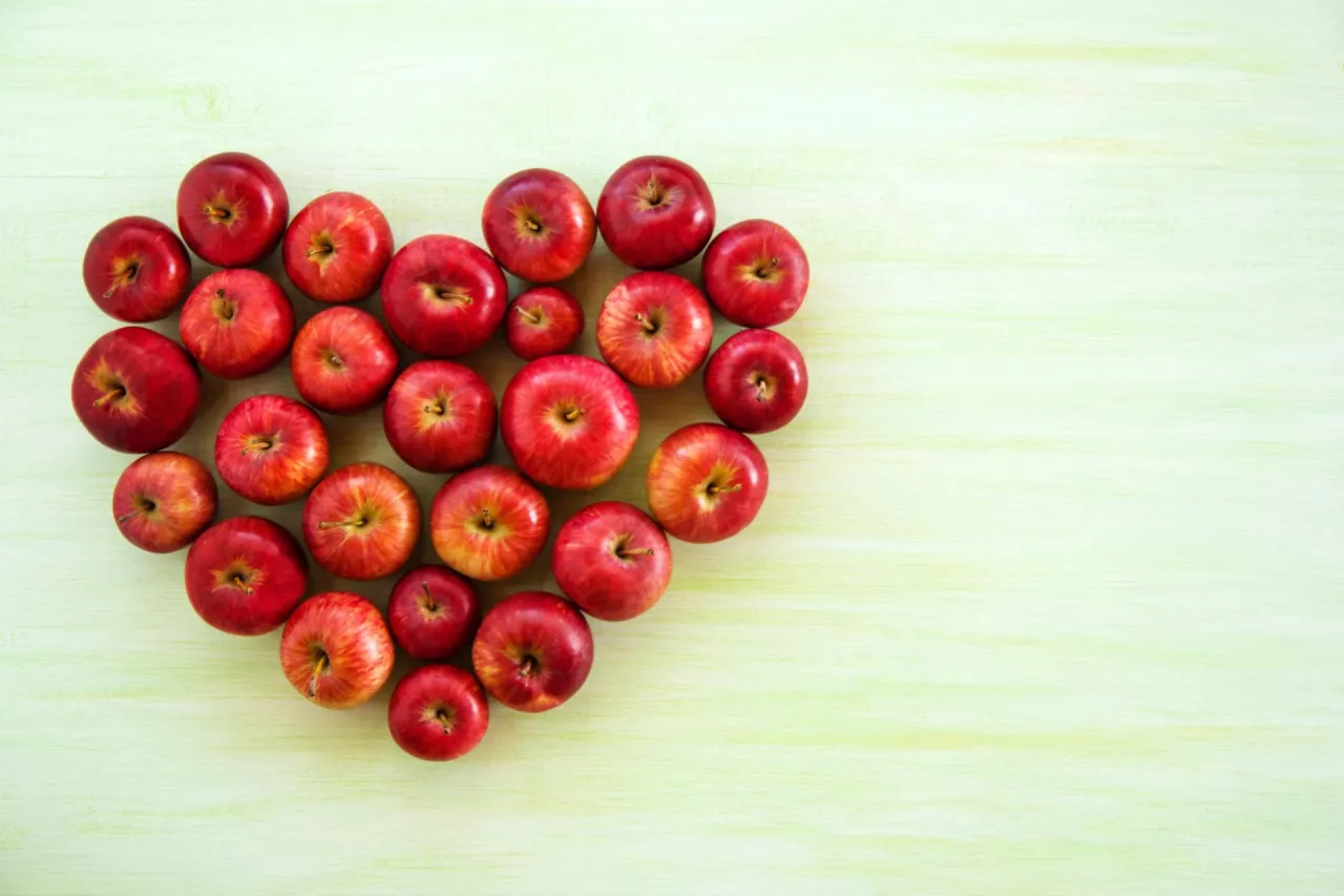 A heart from ripe red apples on the green wooden background, top view.