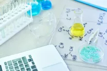 Close up background of working desk in modern science laboratory: test tubes, chemical formulas and laptop on table