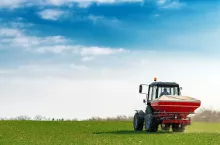 Unrecognizable farmer in agricultural tractor is fertilizing wheat crop field with NPK fertilizer nutrients