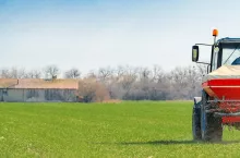 Unrecognizable farmer in agricultural tractor is fertilizing wheat crop field with NPK fertilizer nutrients