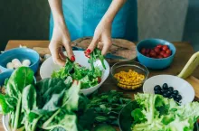 Top view of the kitchen table with ingredients for preparing a salad of European cuisine and the female hands of the cook.