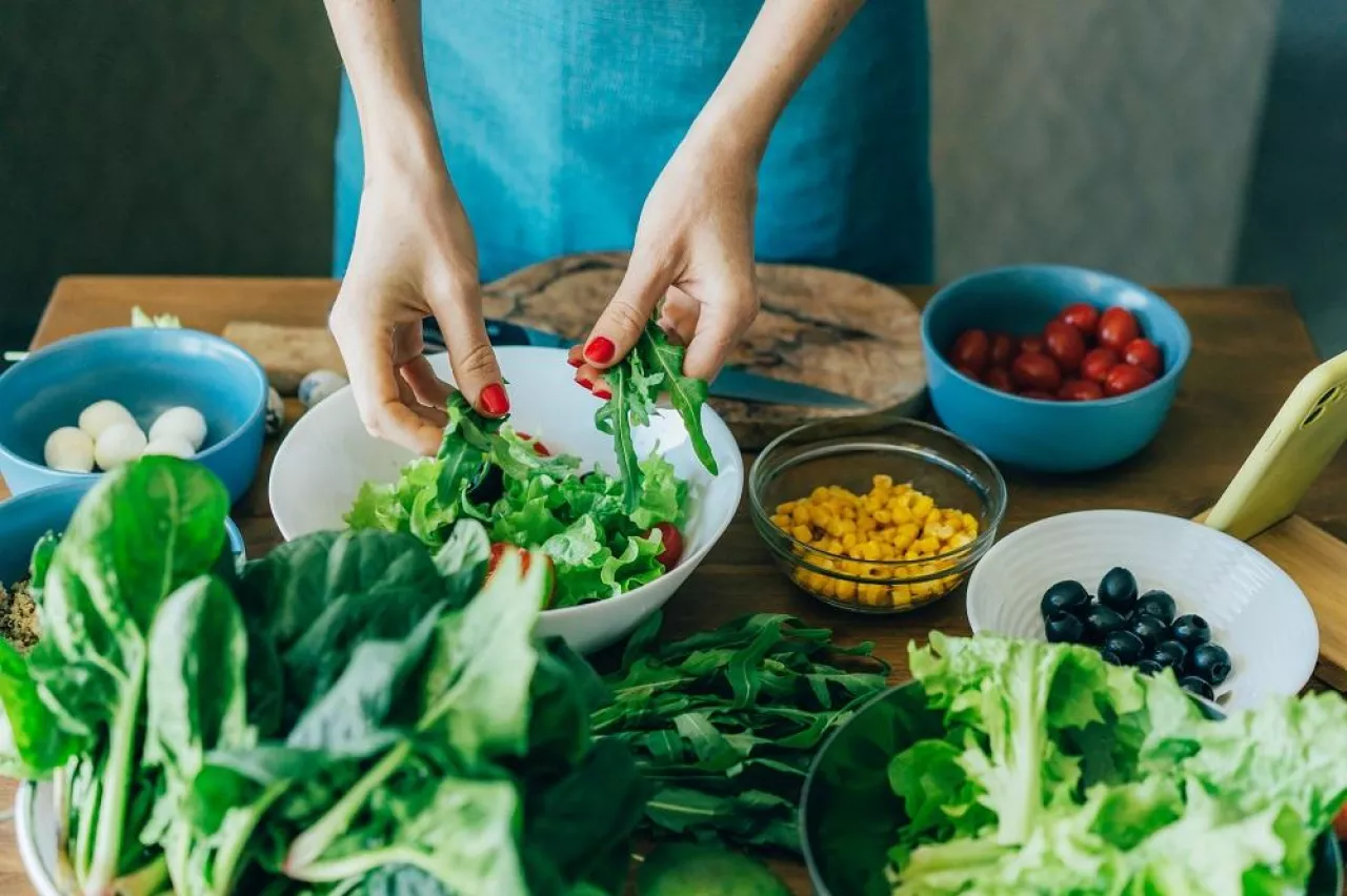 Top view of the kitchen table with ingredients for preparing a salad of European cuisine and the female hands of the cook.