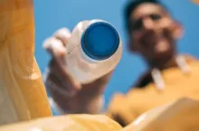 Young man throwing plastic bottles in the trash. Selective focus on bottle in the foreground