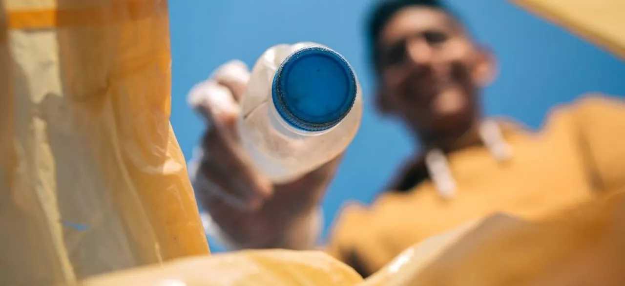 Young man throwing plastic bottles in the trash. Selective focus on bottle in the foreground