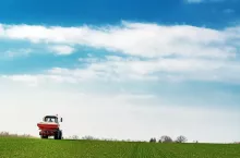Unrecognizable farmer in agricultural tractor is fertilizing wheat crop field with NPK fertilizer nutrients