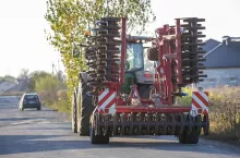 Tractor combine with disc harrows driving along rural road on sunny day. Agricultural machinery and farming concept.