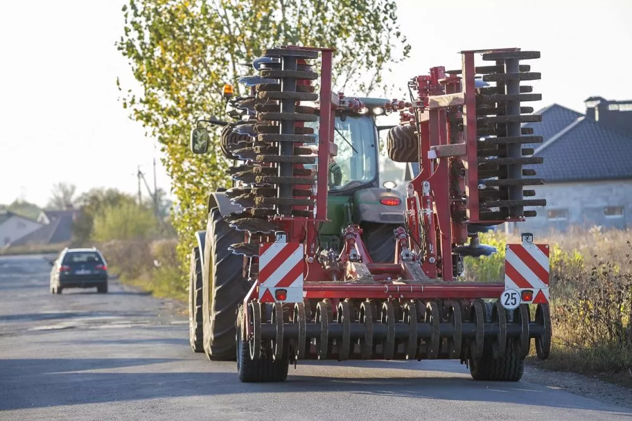 Tractor combine with disc harrows driving along rural road on sunny day. Agricultural machinery and farming concept.