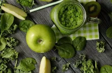 From above shot of green composition with fresh ripe apple and kiwi slices on wooden table with smoothie in jar and fresh greens