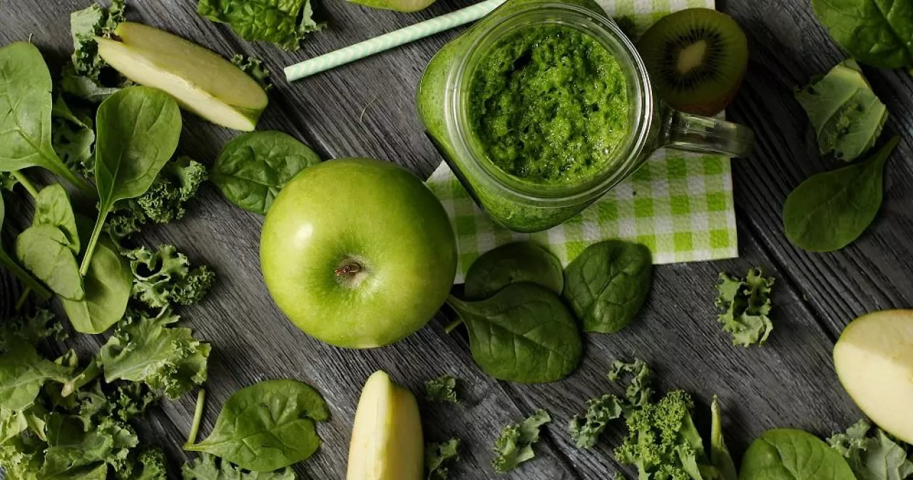 From above shot of green composition with fresh ripe apple and kiwi slices on wooden table with smoothie in jar and fresh greens