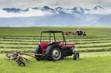 Two red tractors on a farm, working in a field cutting a grass crop.