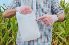 Farmer holding pesticide chemical jug in cornfield. Blank unlabelled bottle as mock up copy space for herbicide, fungicide or insecticide used in corn crop farming.