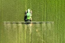 Tractor spraying chemical pesticides with sprayer on the large green agricultural field at spring.