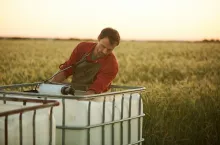 Portrait of male worker washing tools and equipment while standing by water tank in field at sunset, copy space