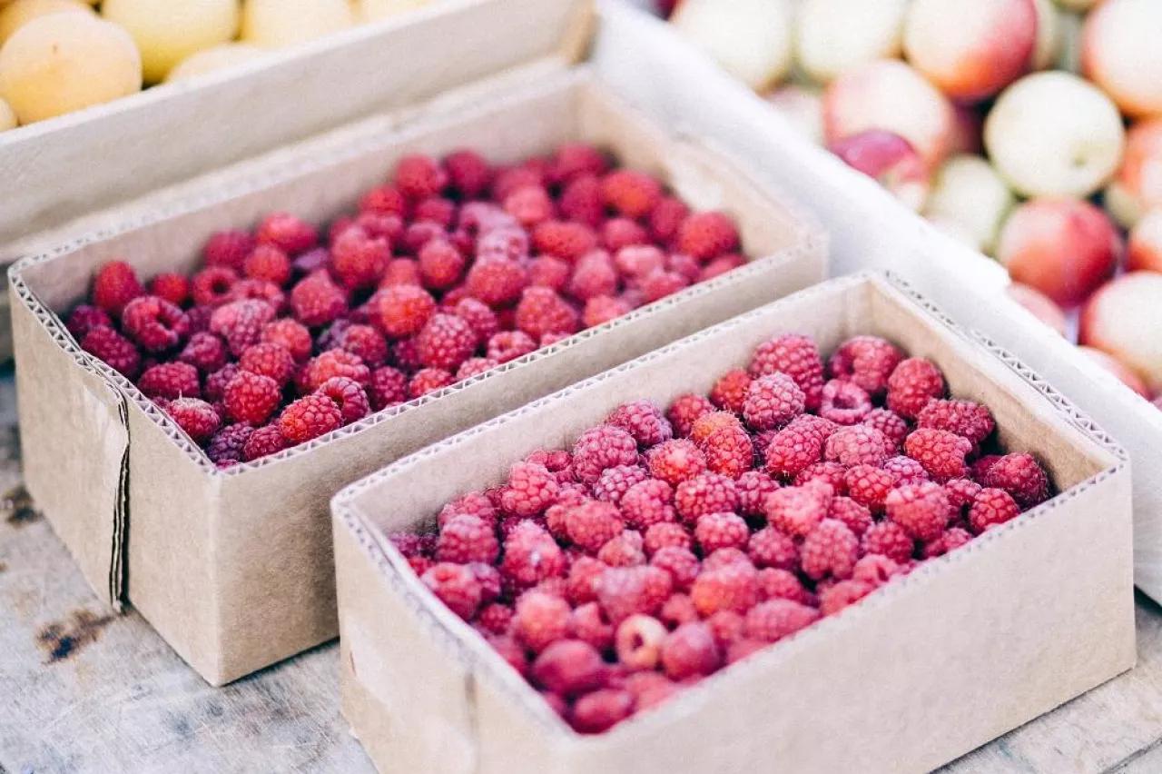 Red raspberries in cardboard boxes for sale. Closeup of ripe raspberries in a box