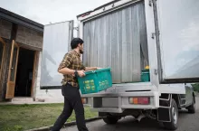 Portrait of a hipster farmer holding box of fruit lift up to the car to go market for sell.