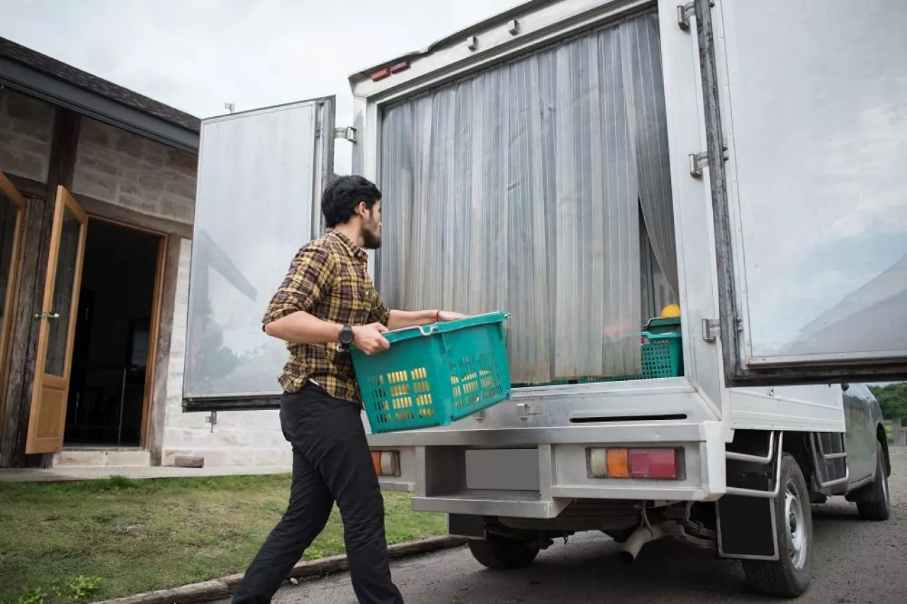Portrait of a hipster farmer holding box of fruit lift up to the car to go market for sell.