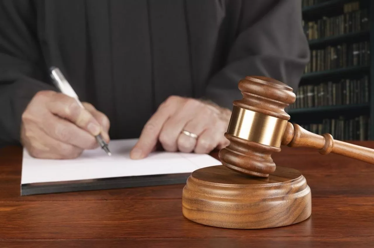 A gavel and block rests on a judge‘s desk while the magistrate takes notes in his law library preparing to oversee a case.